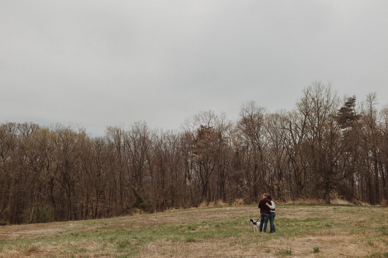 couple embraces in field with dog at engagement session