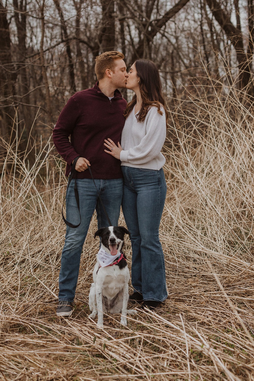 couple kisses while holding dog at engagement session