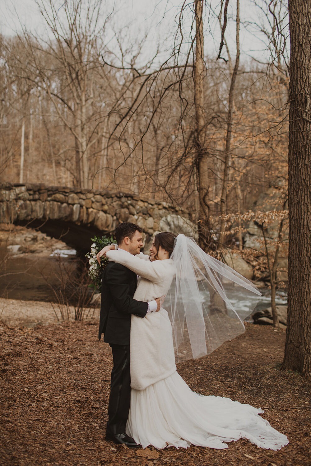 couple embraces beside bridge for Rock Creek Park photos