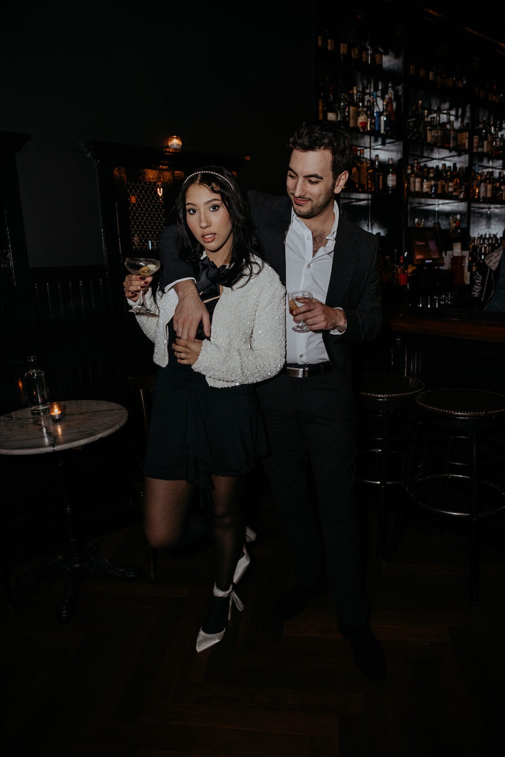 couple holds drinks at bar engagement session 