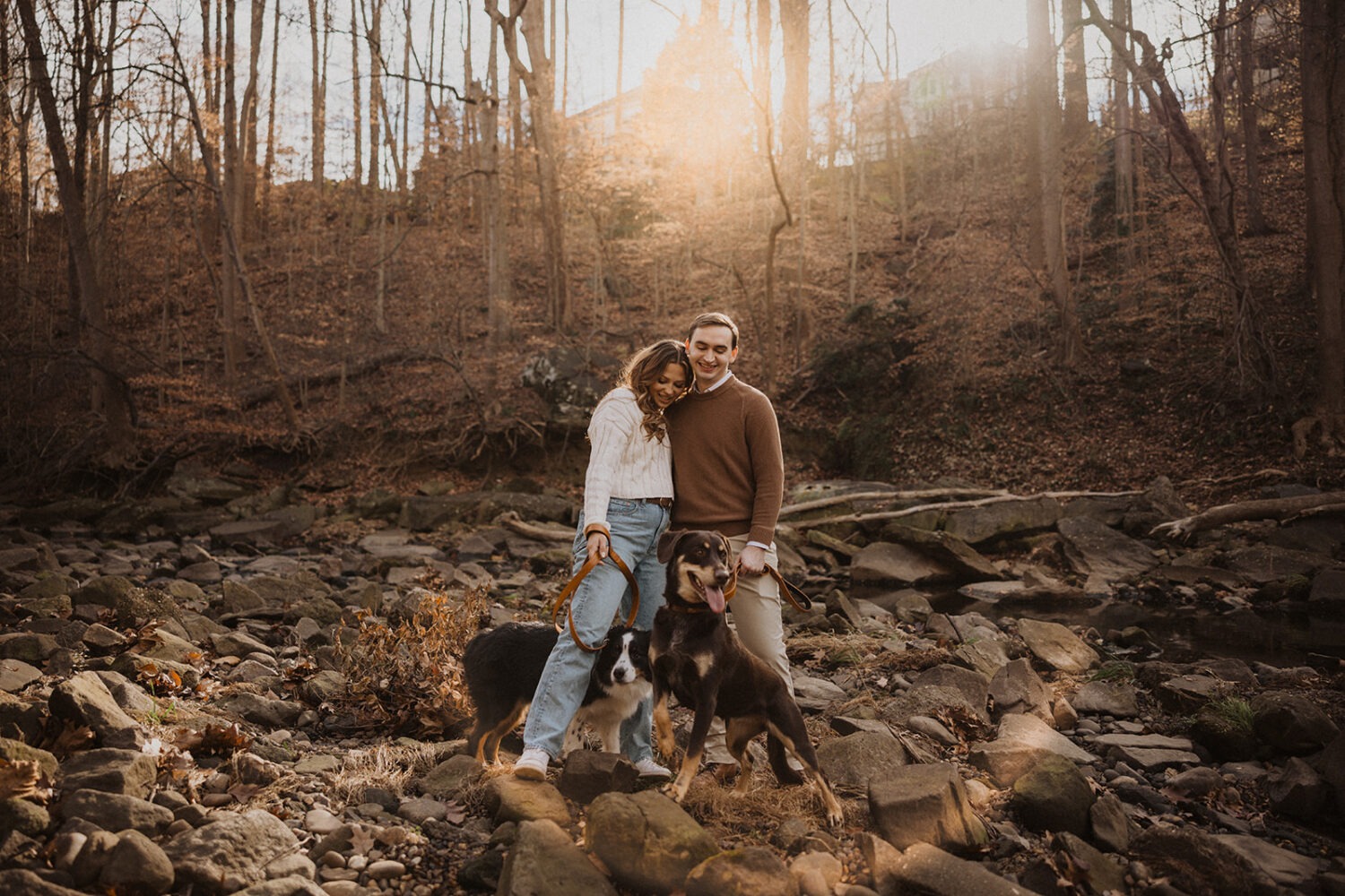 couple stands with dogs at sunset outdoor park engagement session 