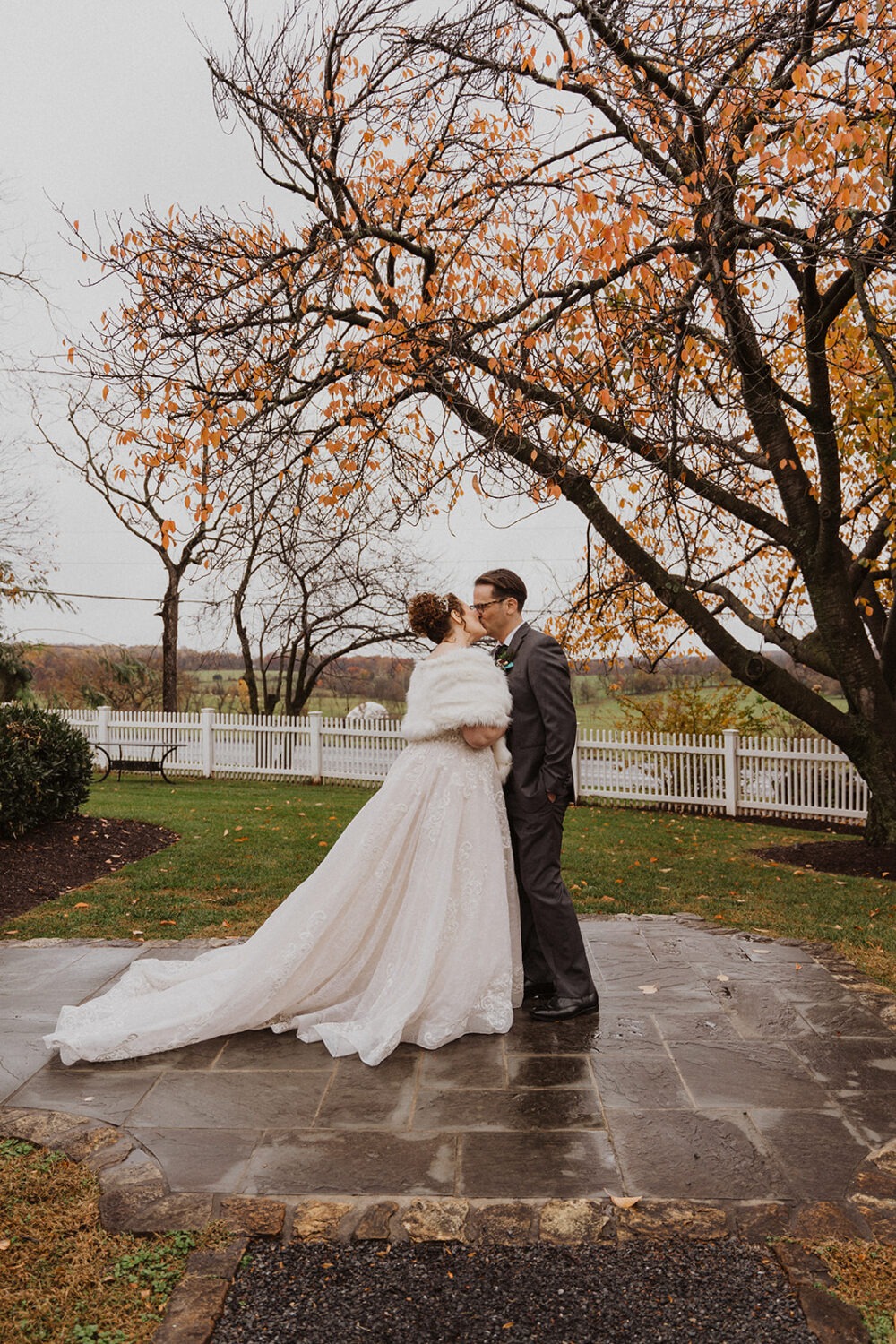 couple kisses under fall leaves on wedding day