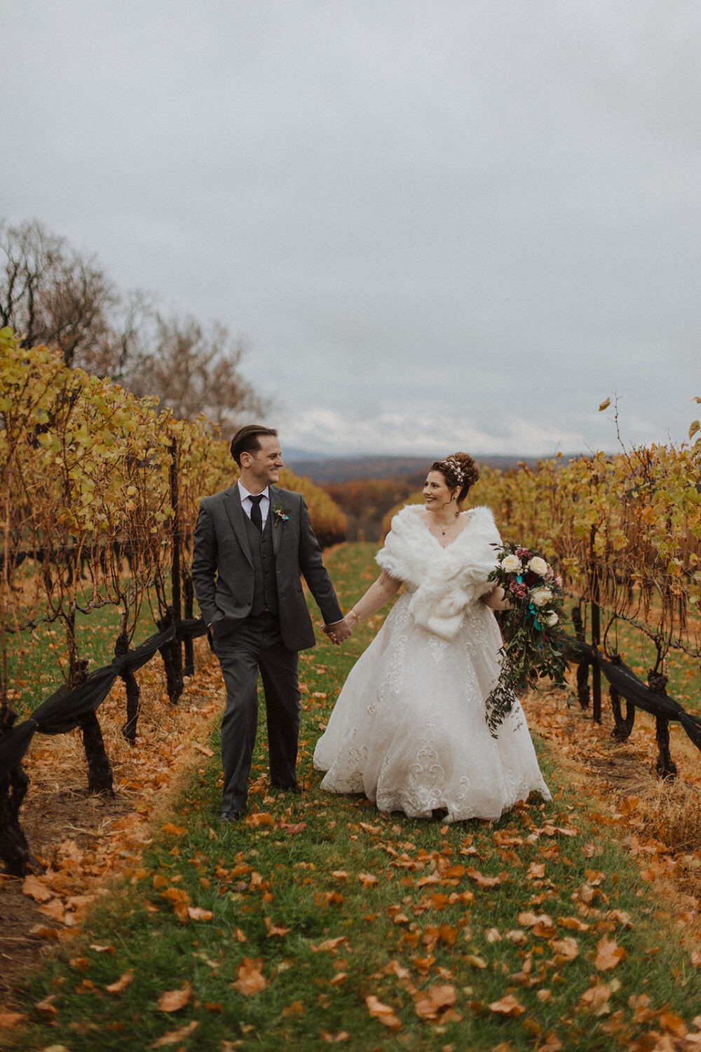 couple walks through vineyard holding hands 
