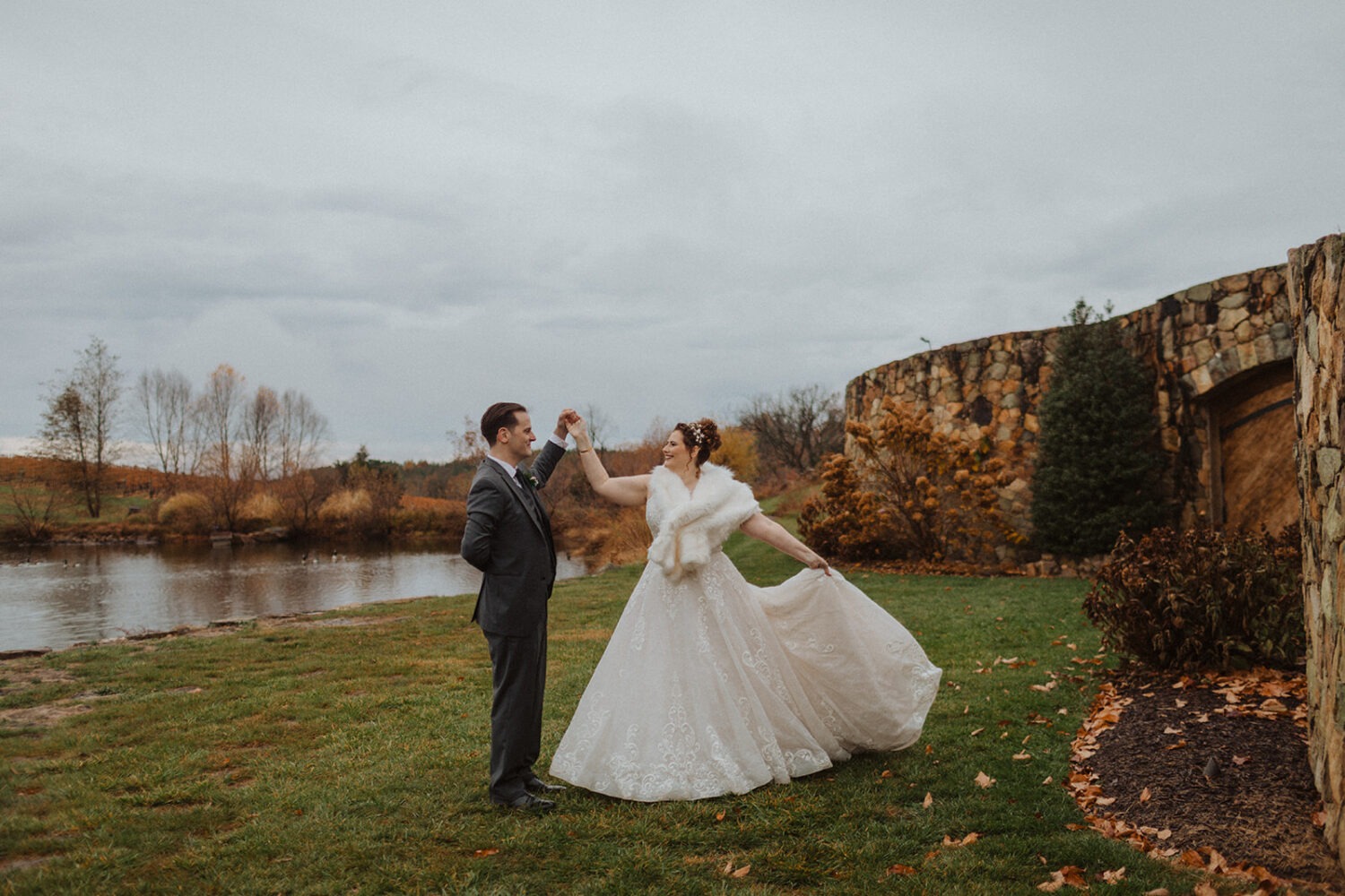 couple twirls beside lake at outdoor wedding 
