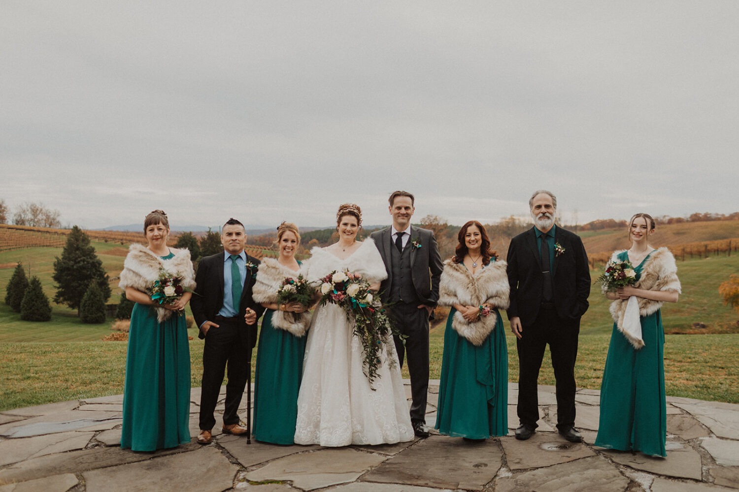couple stands with wedding party at outdoor wedding venue 