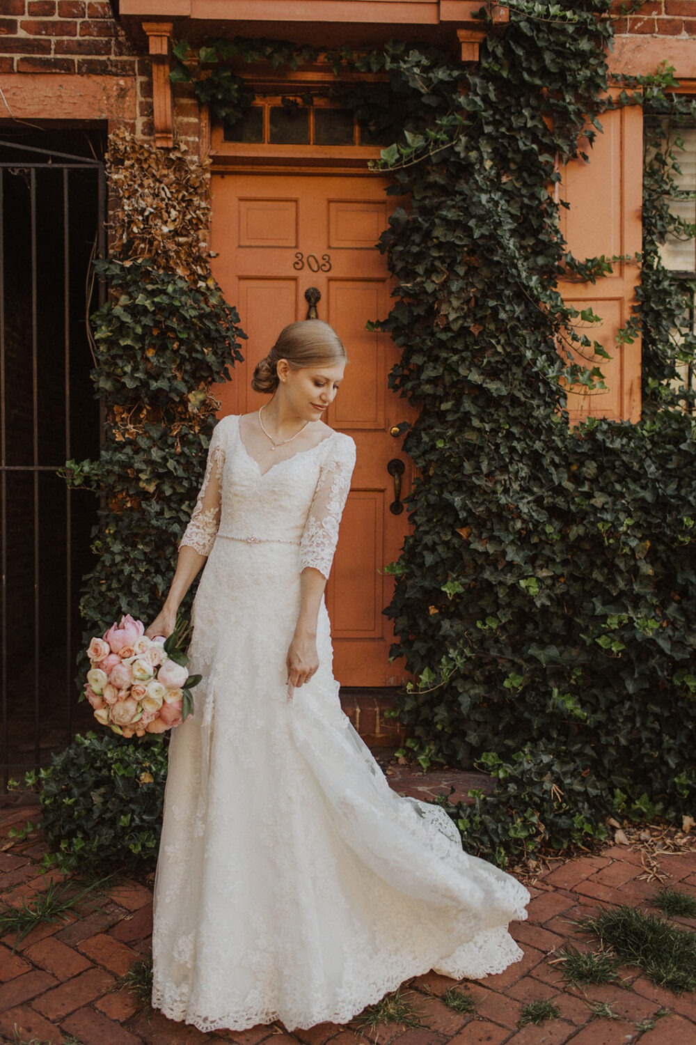 bride poses with pink wedding bouquet in front of door