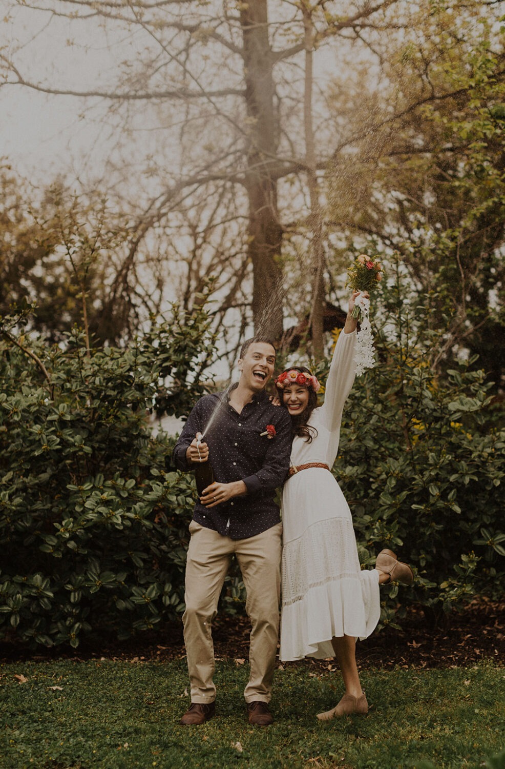 couple pops open champagne at spring engagement photos