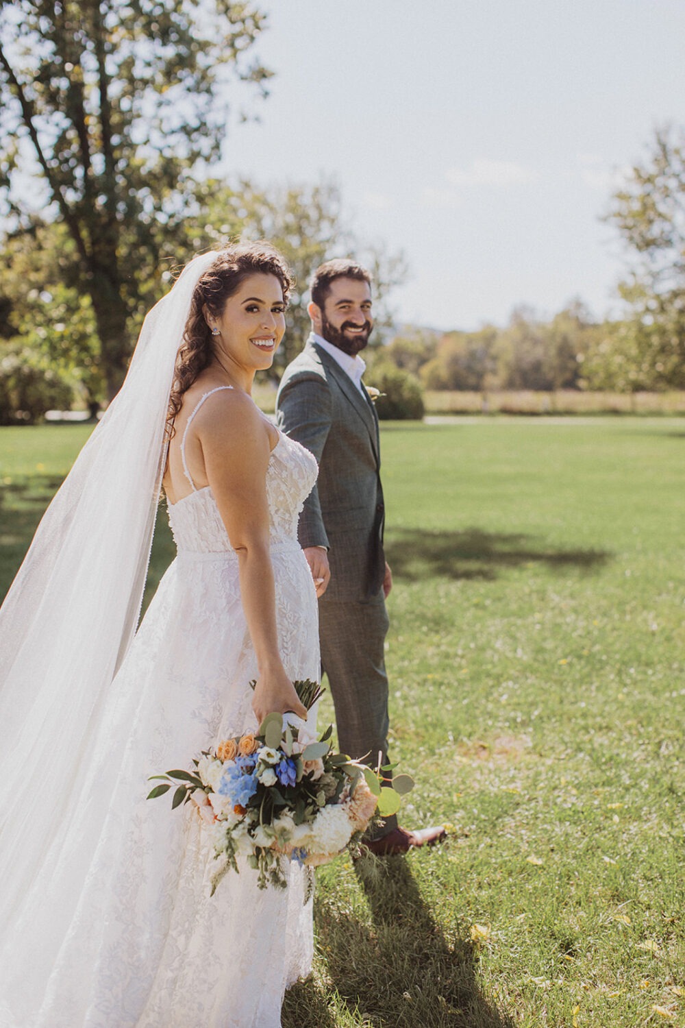 couple walks through field holding hands at outdoor wedding 