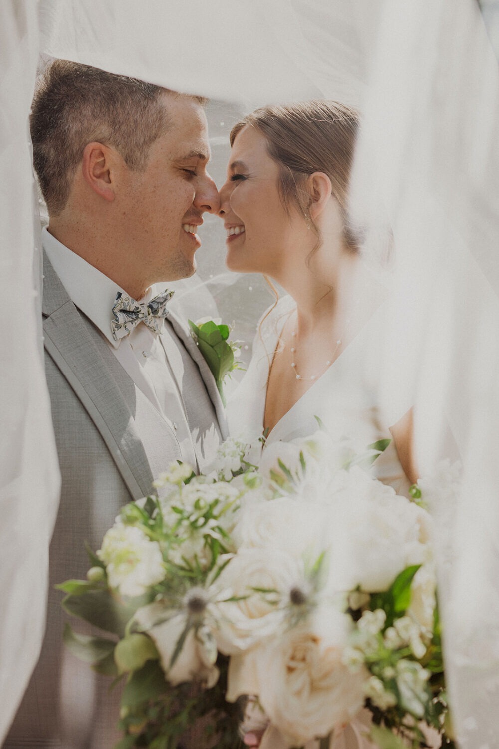 couple kisses under veil holding wedding bouquet