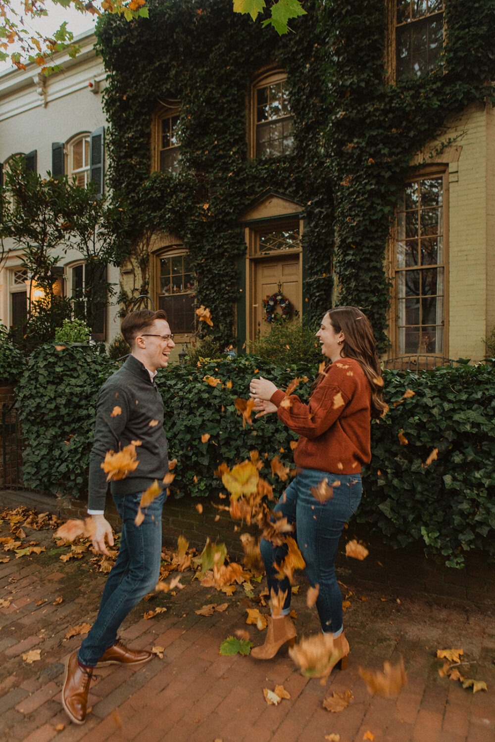 couple throws leaves during fall Georgetown engagement shoot photos