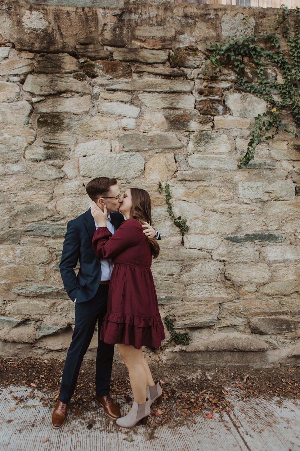 couple kisses in front of ivy-covered wall