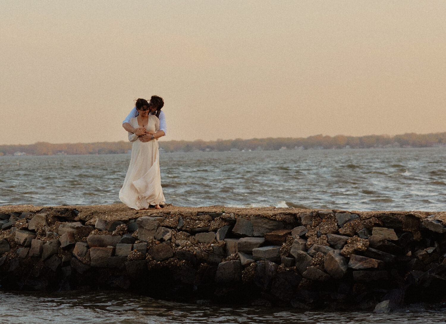 couple kisses on rocks at beach engagement session