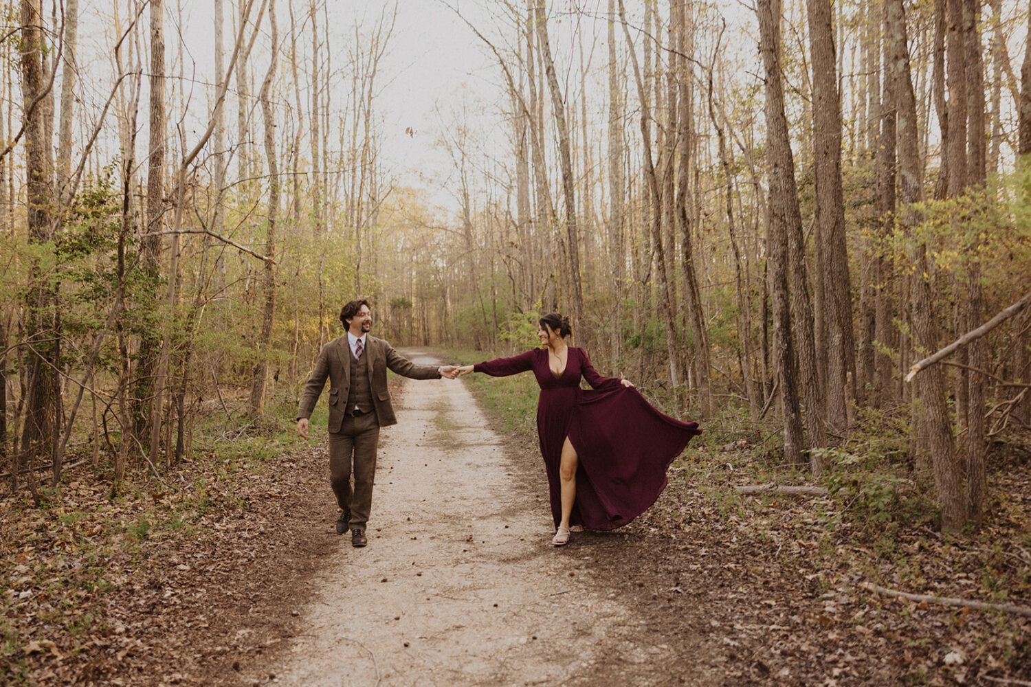 couple walks holding hands through woods engagement session