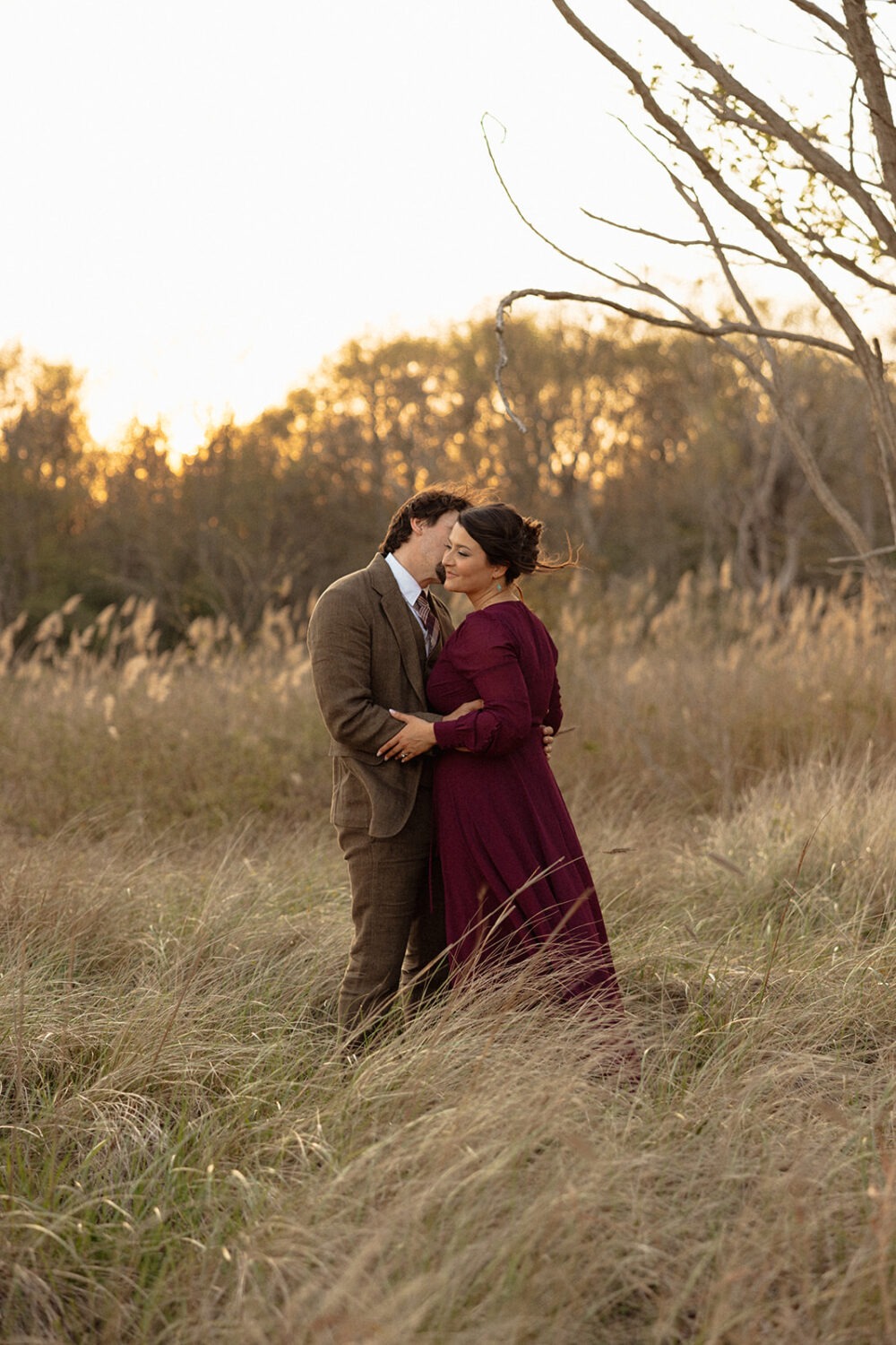 couple kisses in field at sunset engagement session