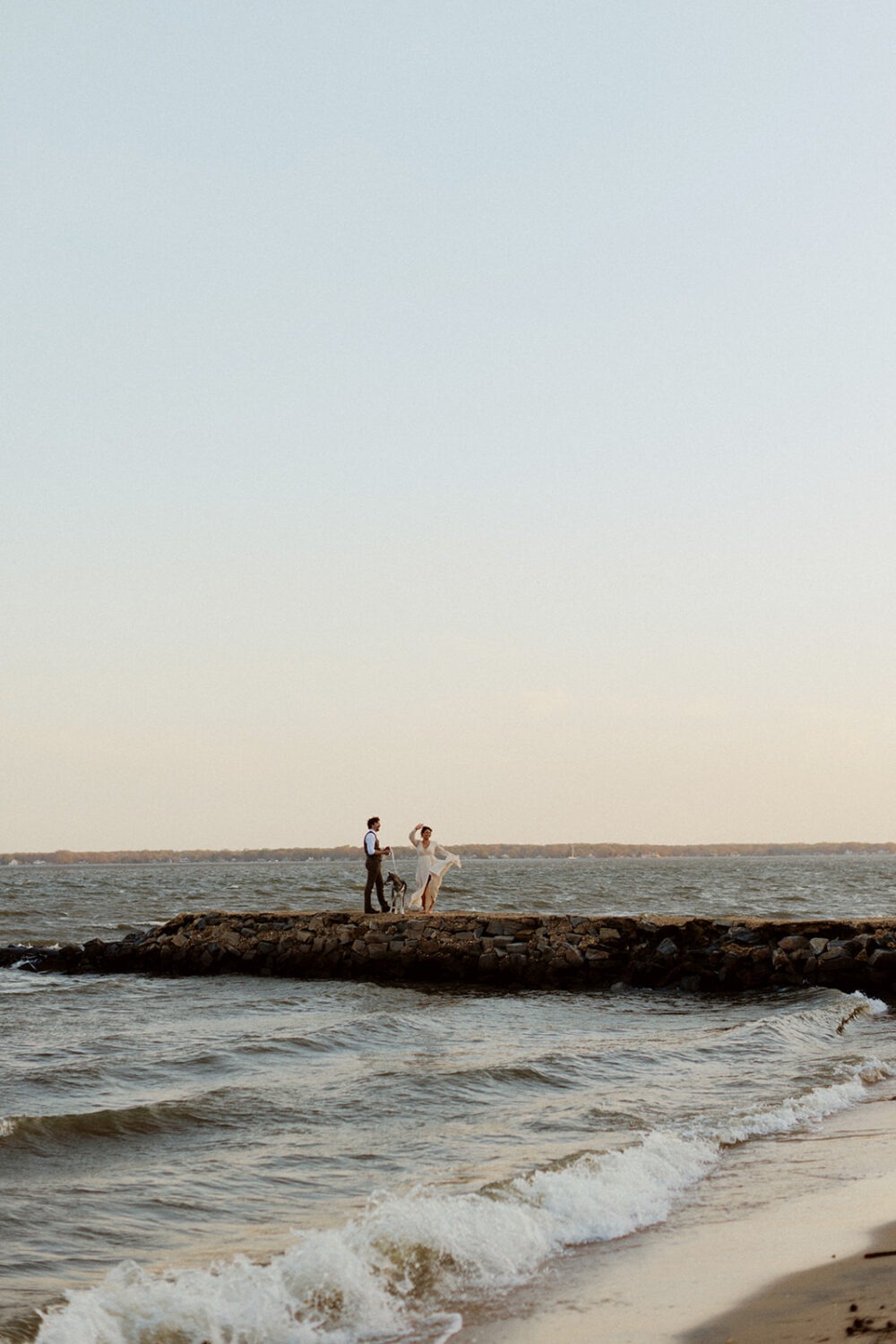 couple walks along rocks at beach photo shoot