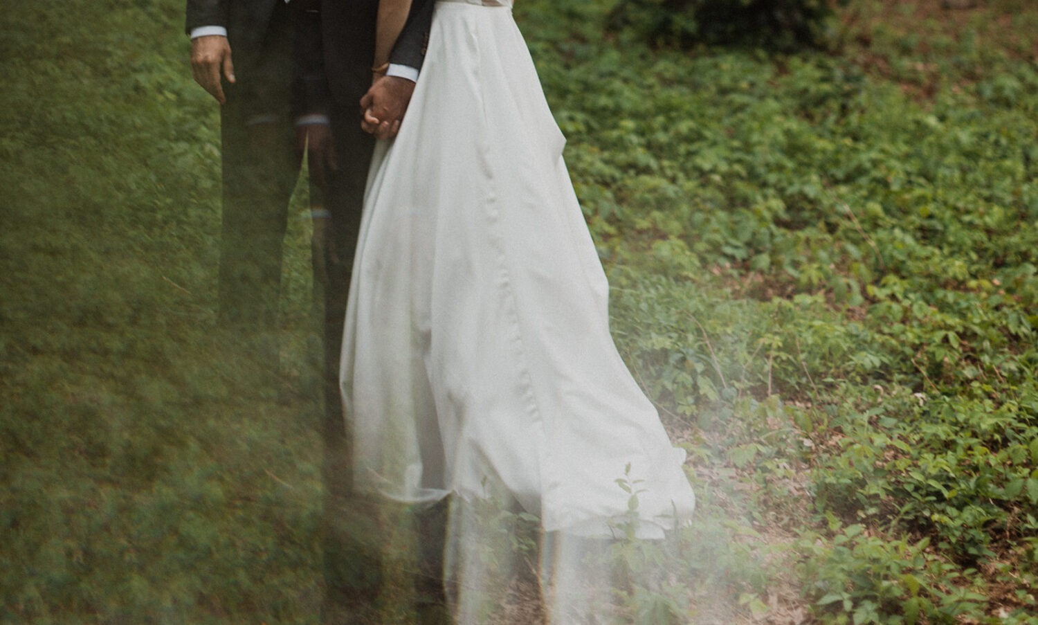 couple holds hands in green woods 