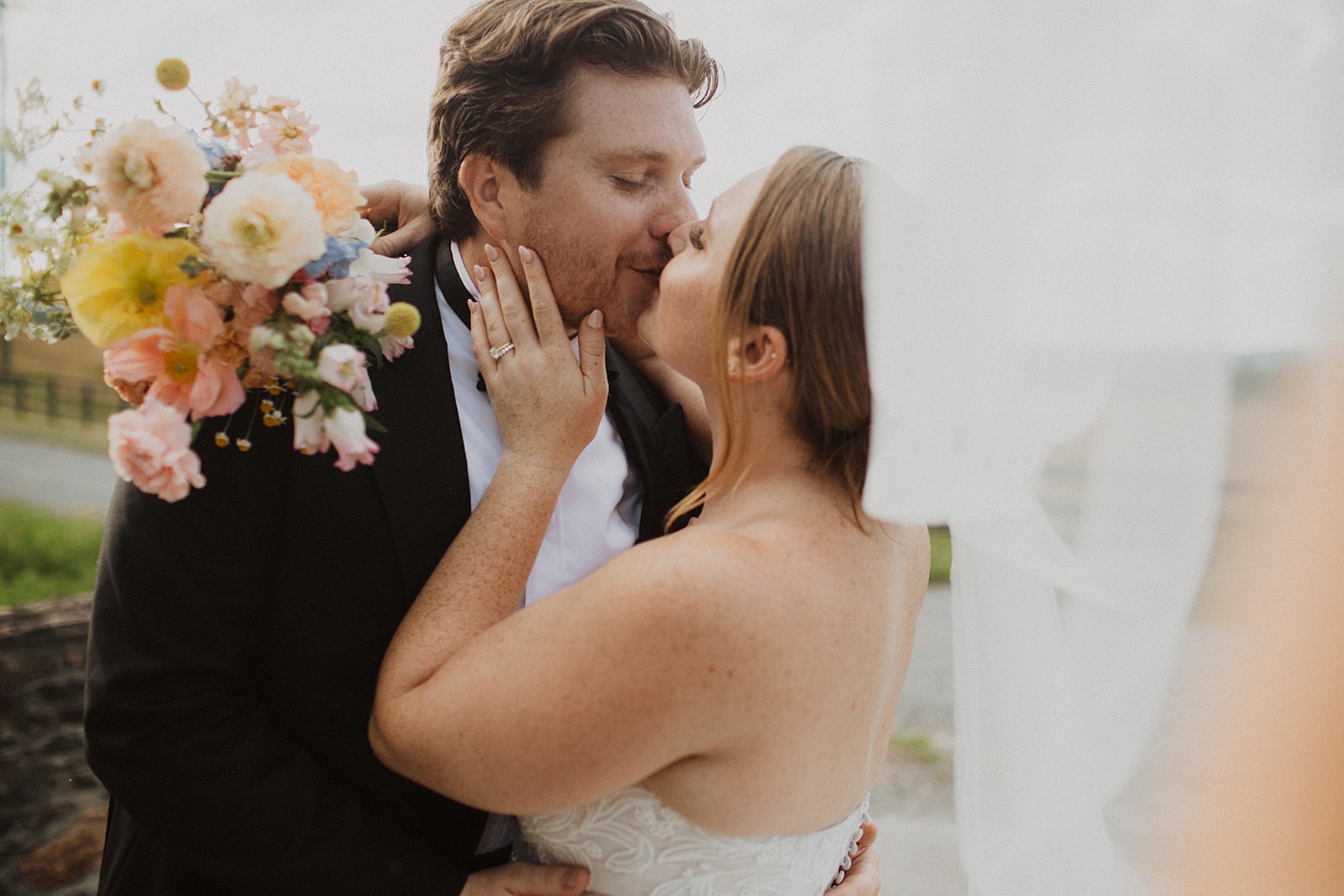 couple kisses under veil holding wedding bouquet