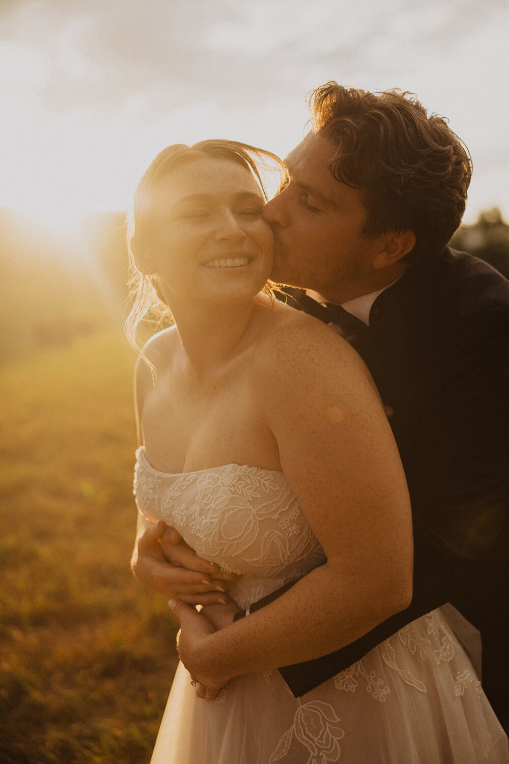 groom kisses bride at outdoor field sunset wedding venue