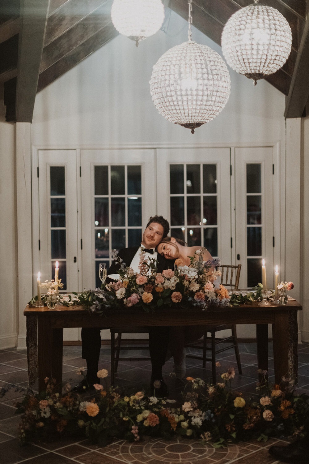 couple snuggles together at floral wedding reception table 