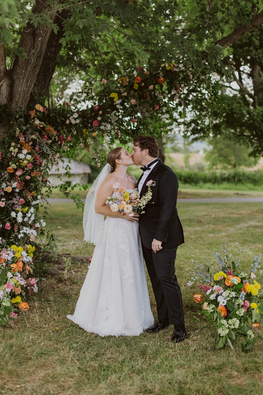 couple kisses surrounded by wedding florals at backyard wedding