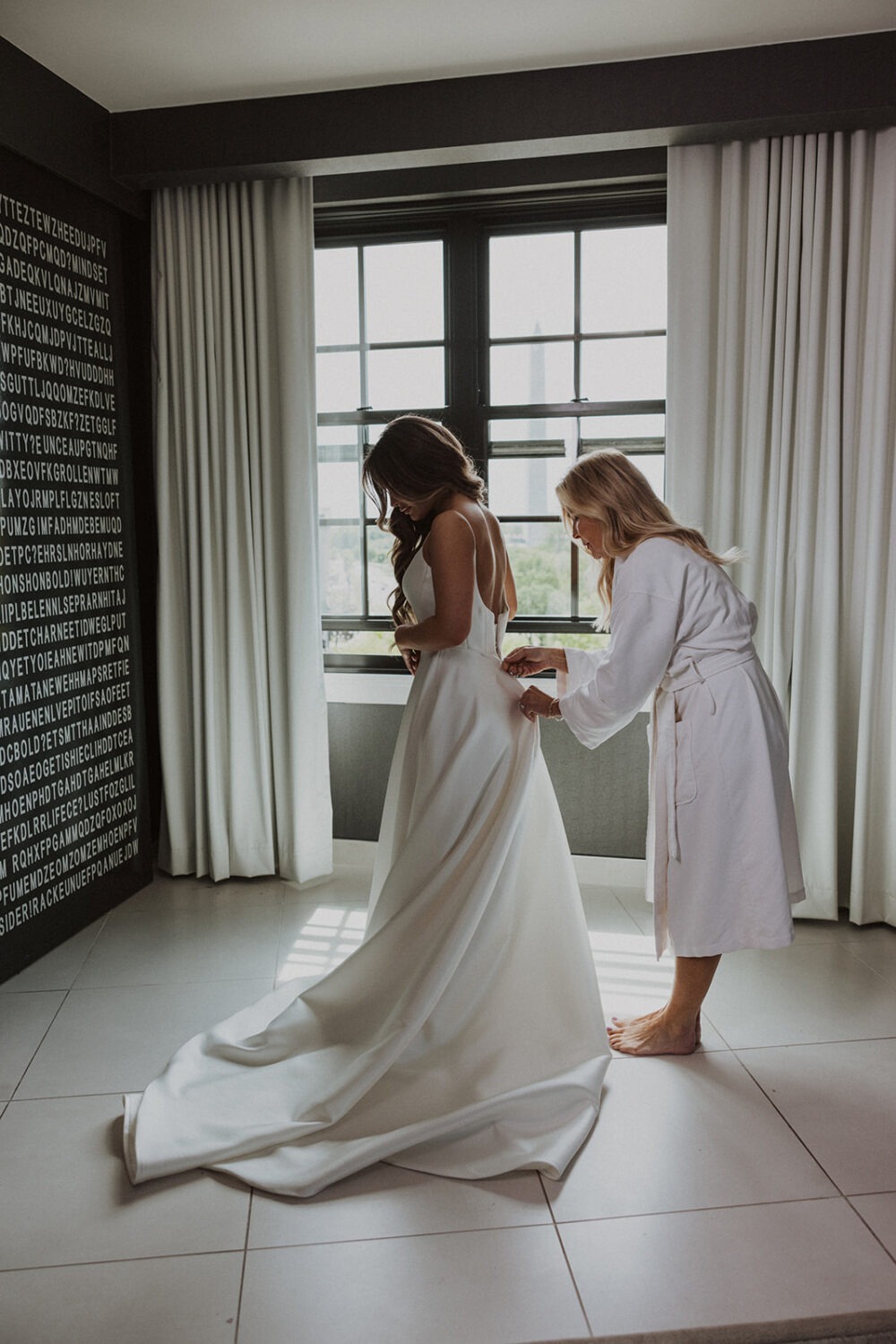 bridesmaid zips up bride's white wedding dress