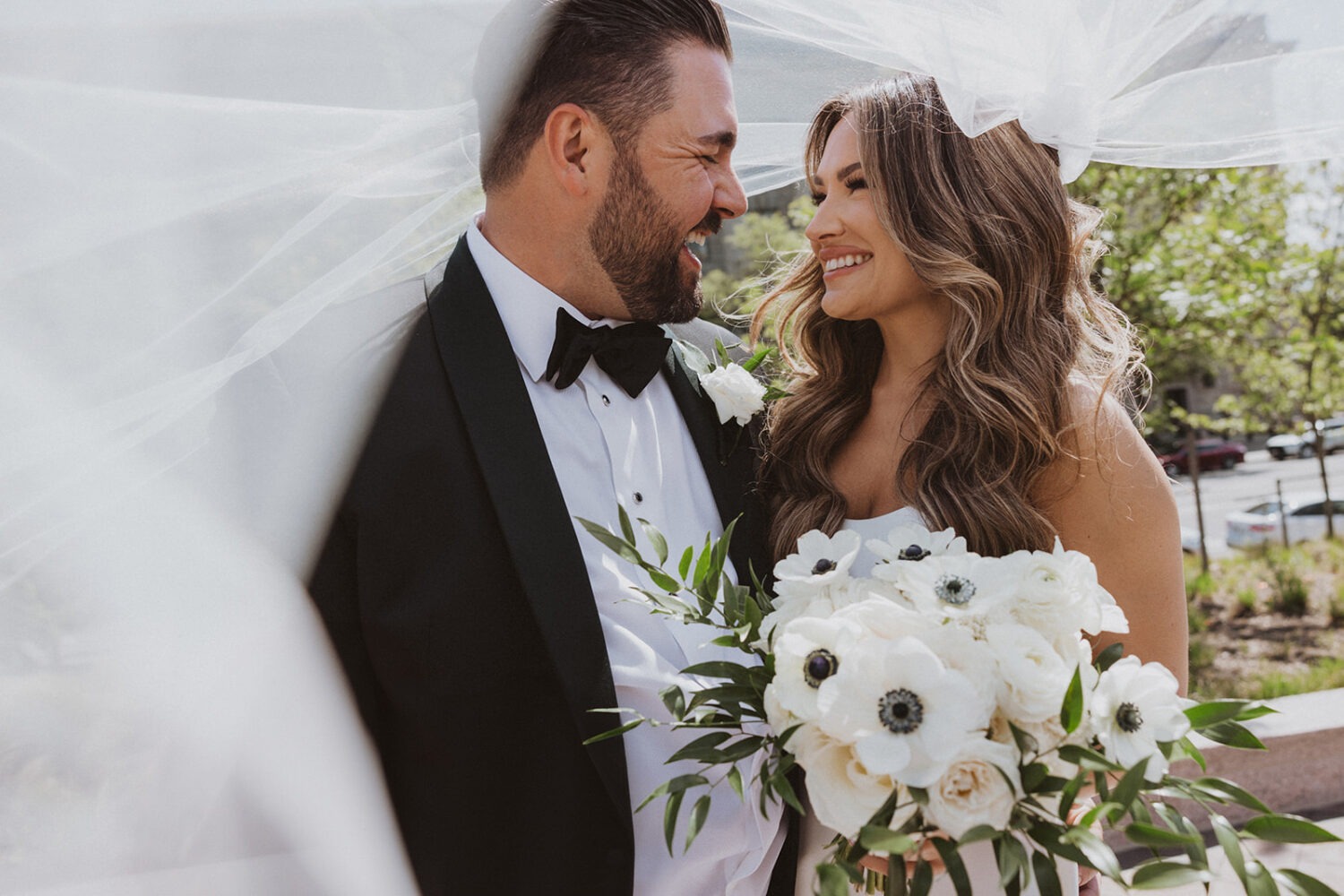 couple laughs under wedding bouquet 