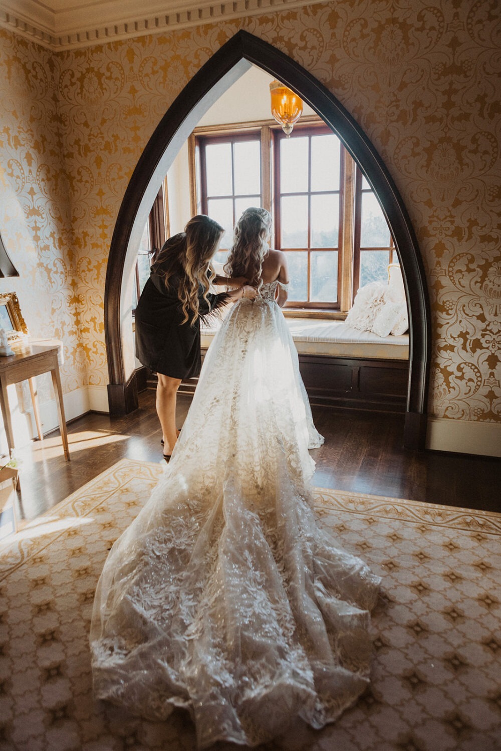 bride has wedding dress buttoned by bridesmaid