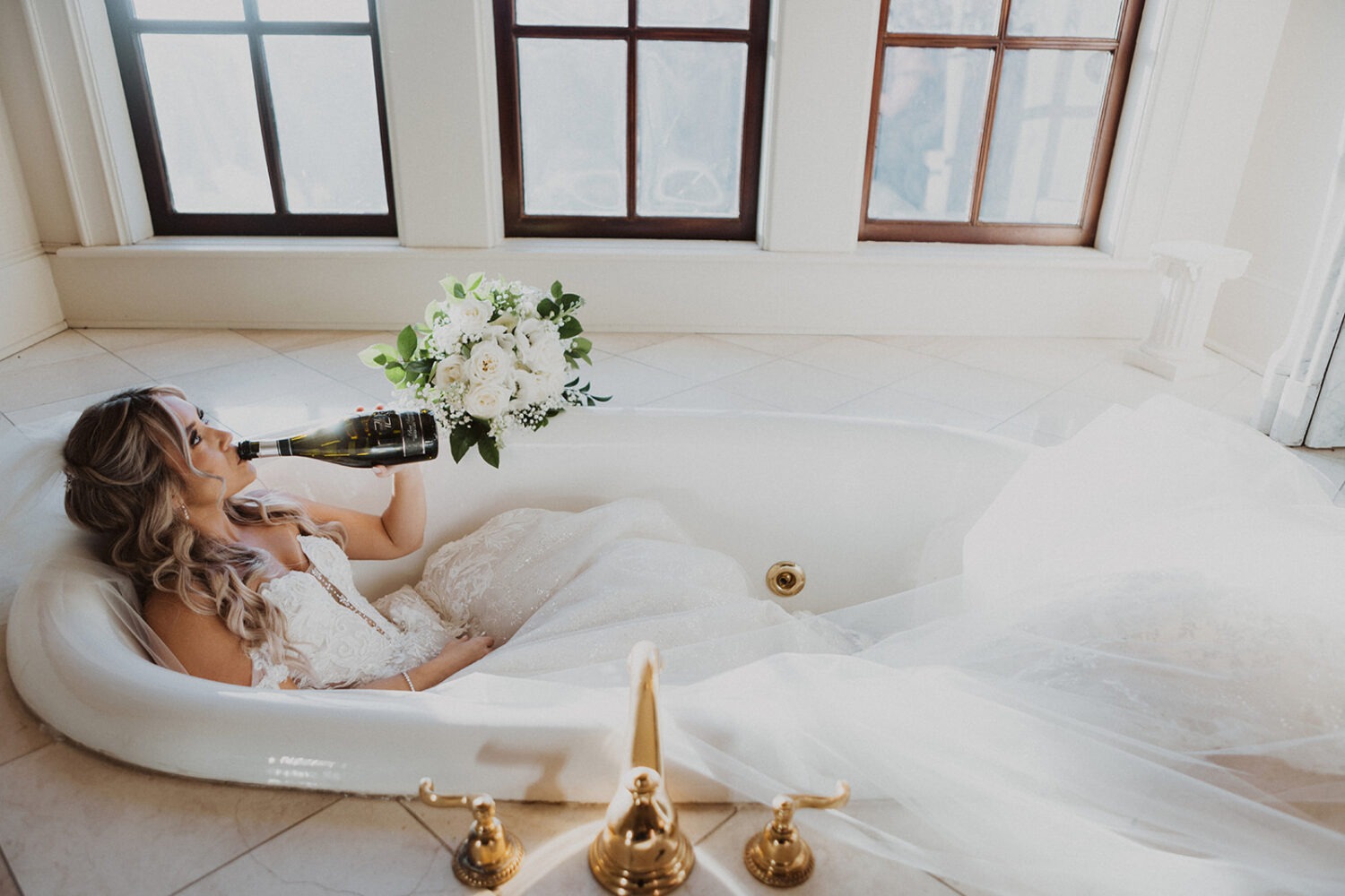 bride holds wedding bouquet in tub of bridal suite