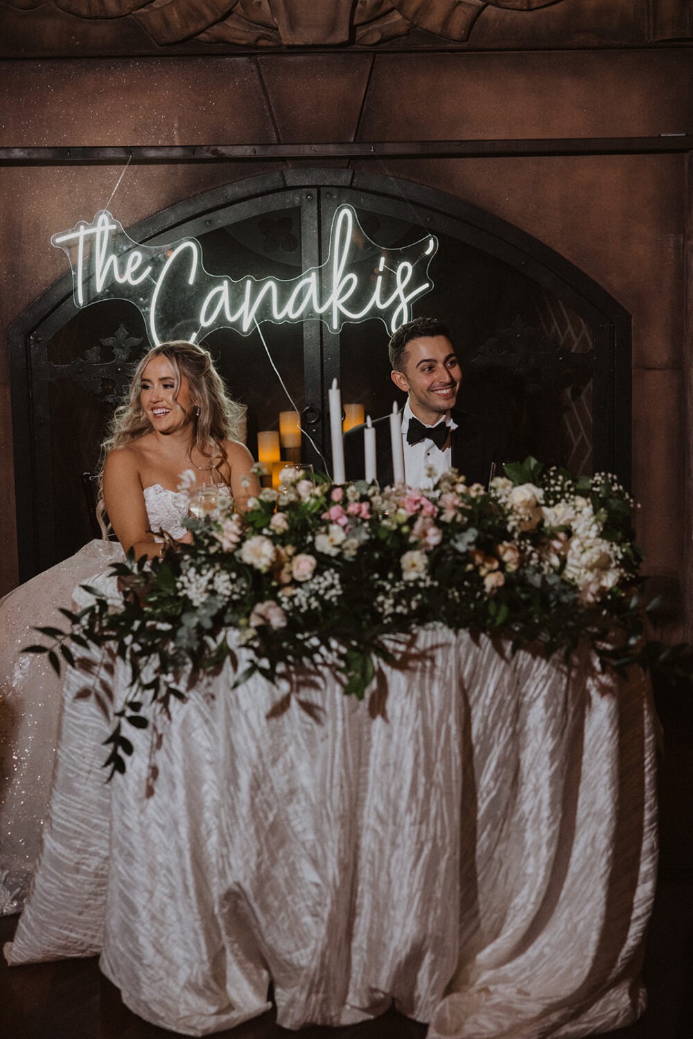 couple sits under neon sign at reception head table