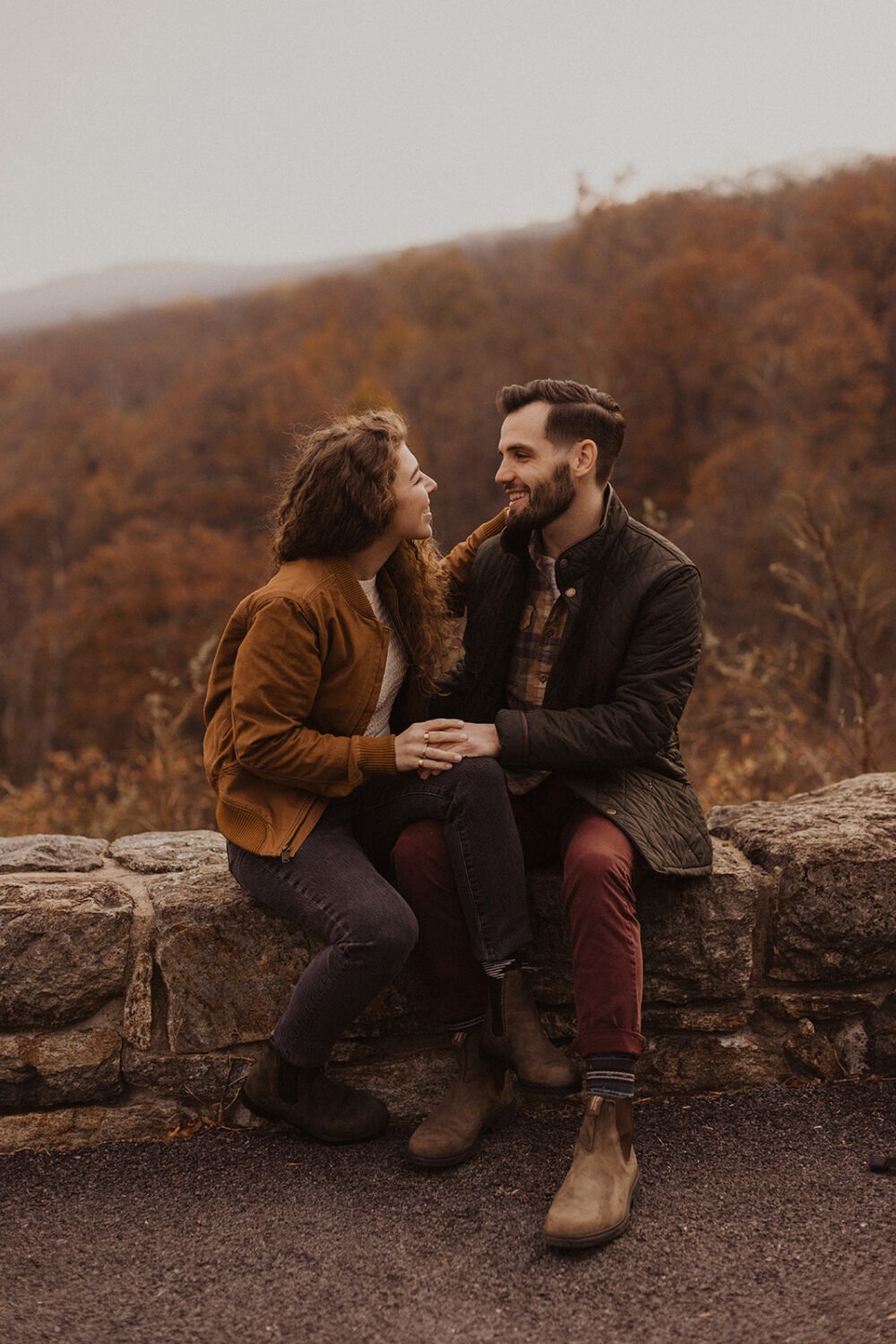 couple sits on overlook at Shenandoah fall engagement photos