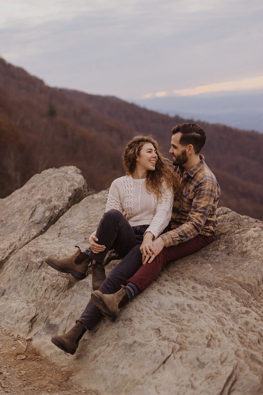 couple sits on overlook at Shenandoah fall engagement photos