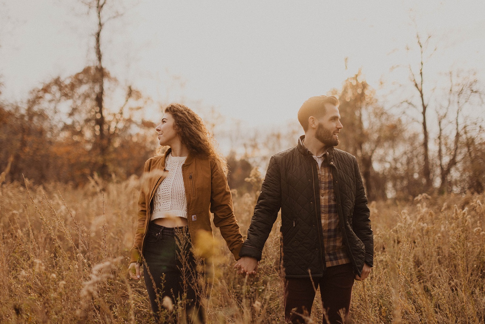 couple holds hands in field during sunset engagement