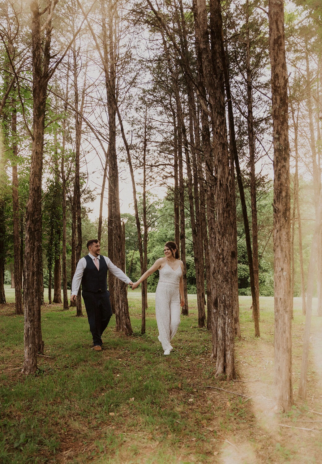 couple walks holding hands at sunset forest wedding