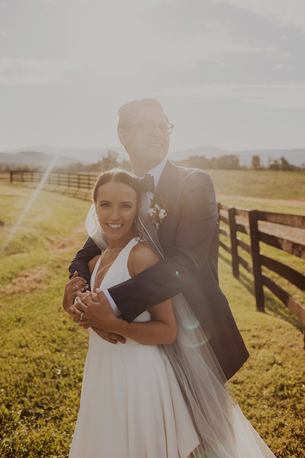 couple embraces in meadow at sunset wedding