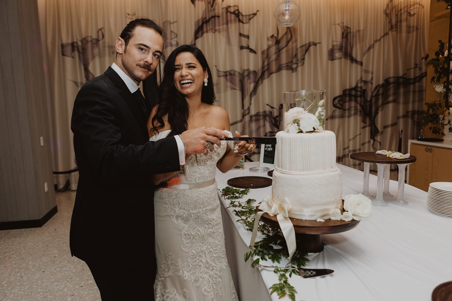 couple cuts white wedding cake during reception