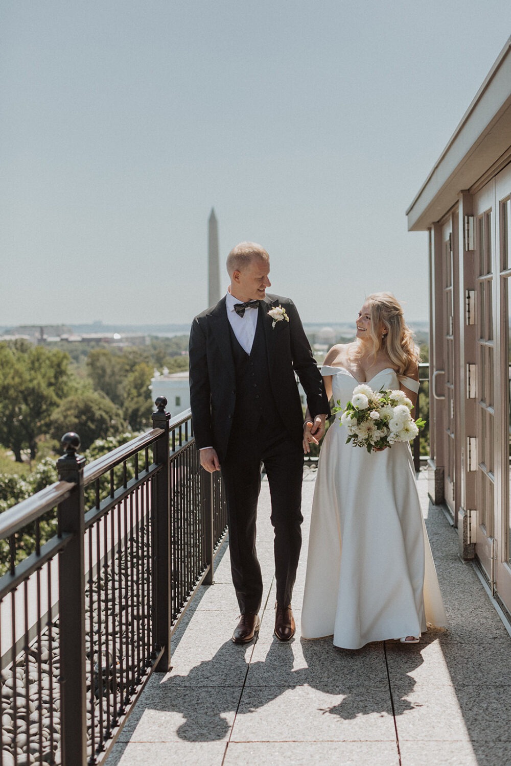 Bride and groom walking on balcony looking at each other smiling.