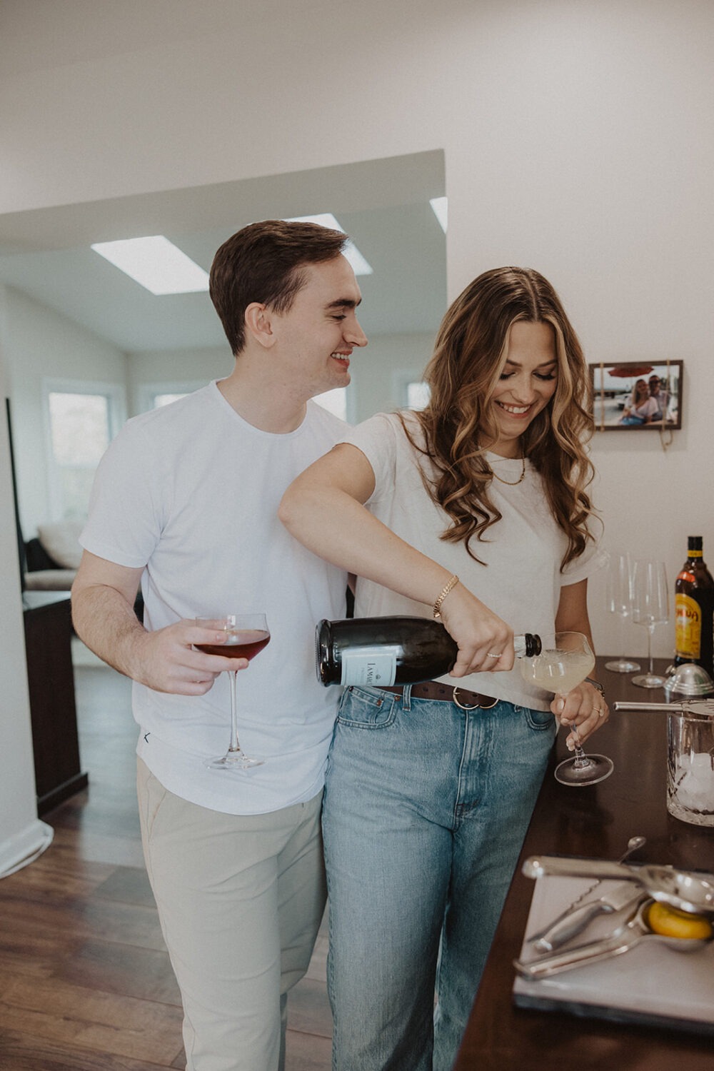 couple pours drinks together at home engagement session