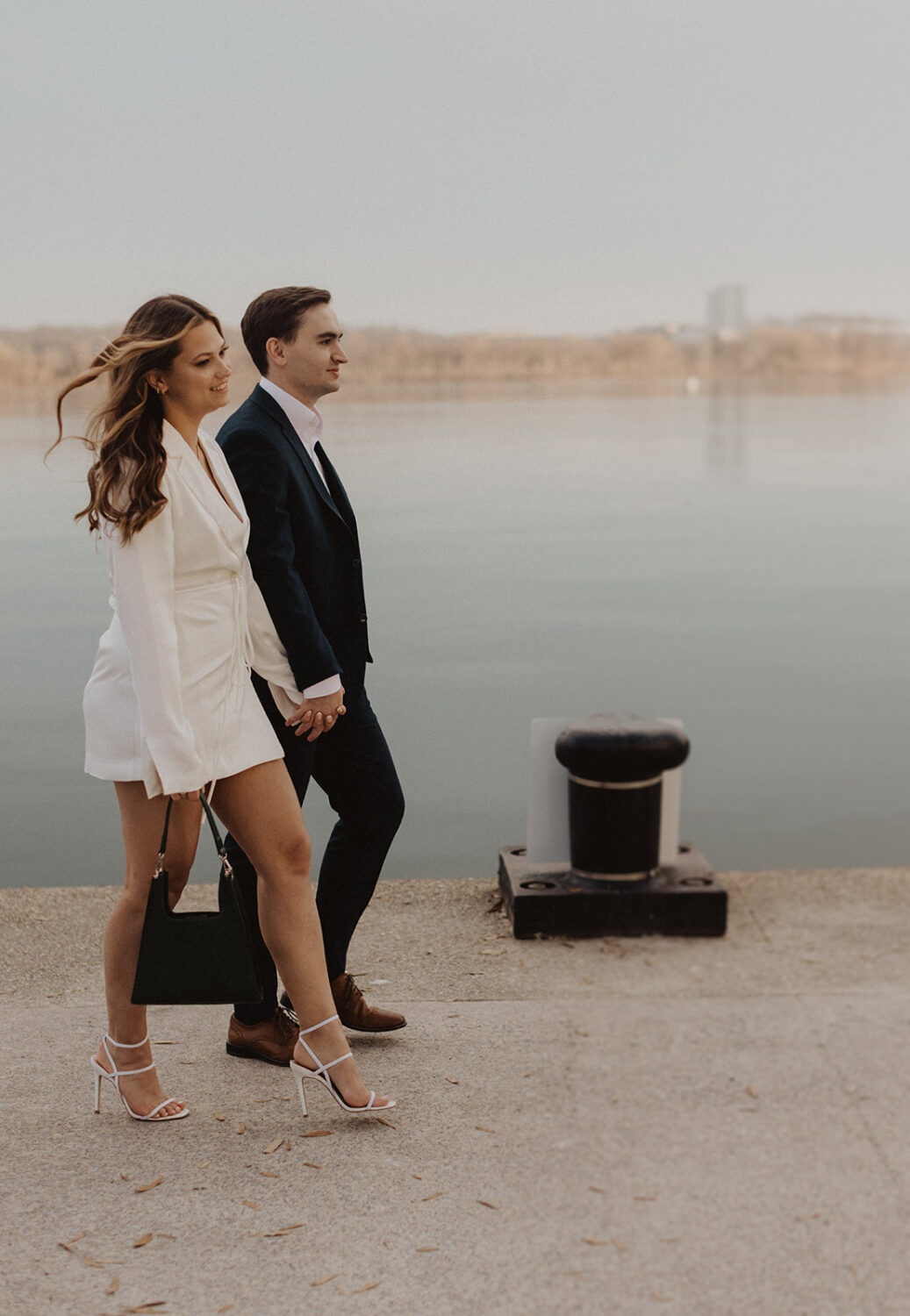 couple walks along waterfront at winter engagement photoshoot