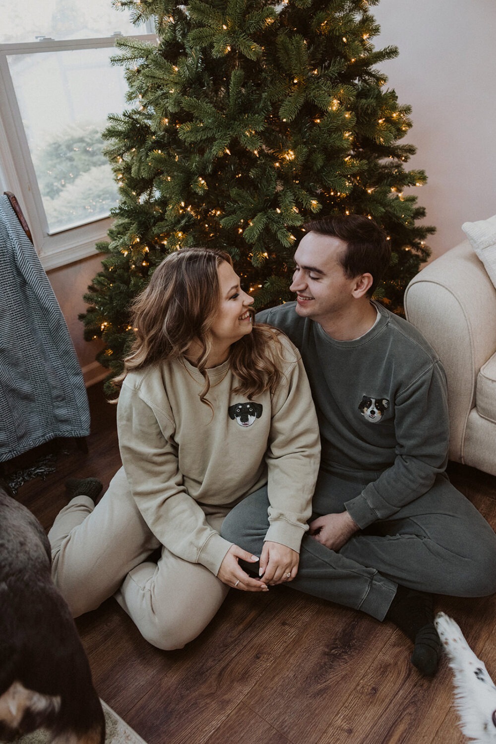 couple sits in front of Christmas tree at winter engagement photoshoot