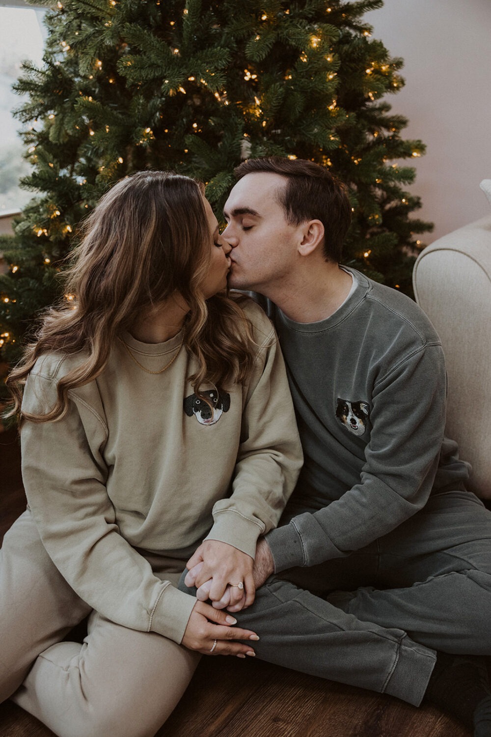 couple kisses in front of Christmas tree in matching sweatsuits