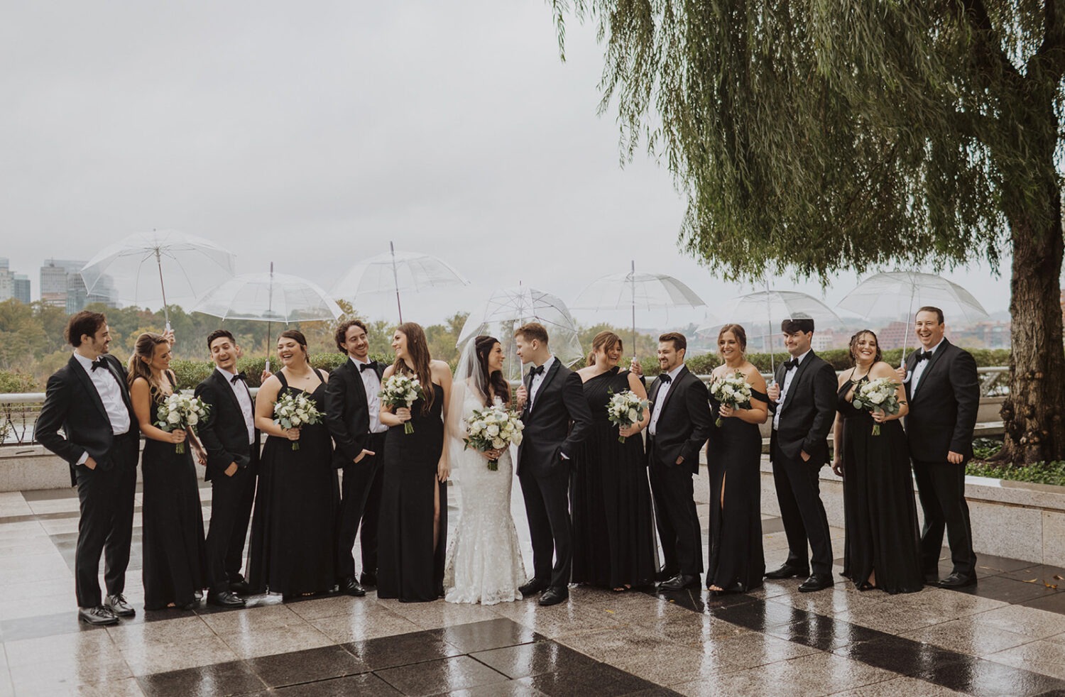 couple poses under umbrellas with wedding party at rainy outdoor DC elopement