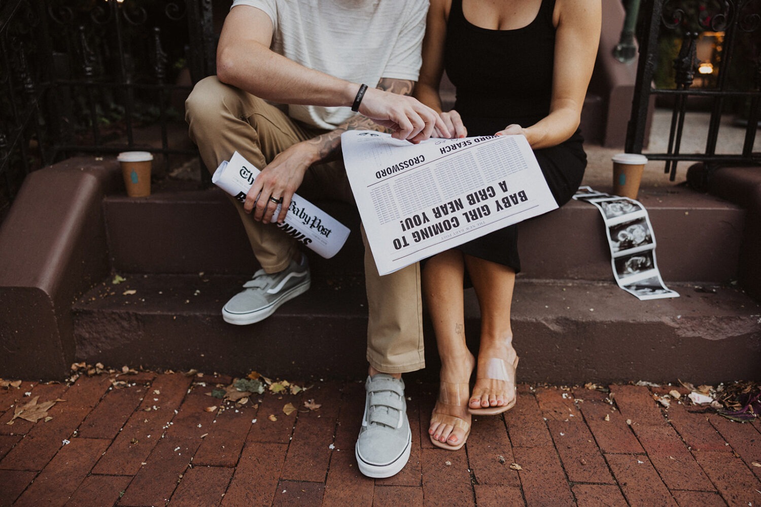 couple holds hands and reads through baby announcement newspaper 