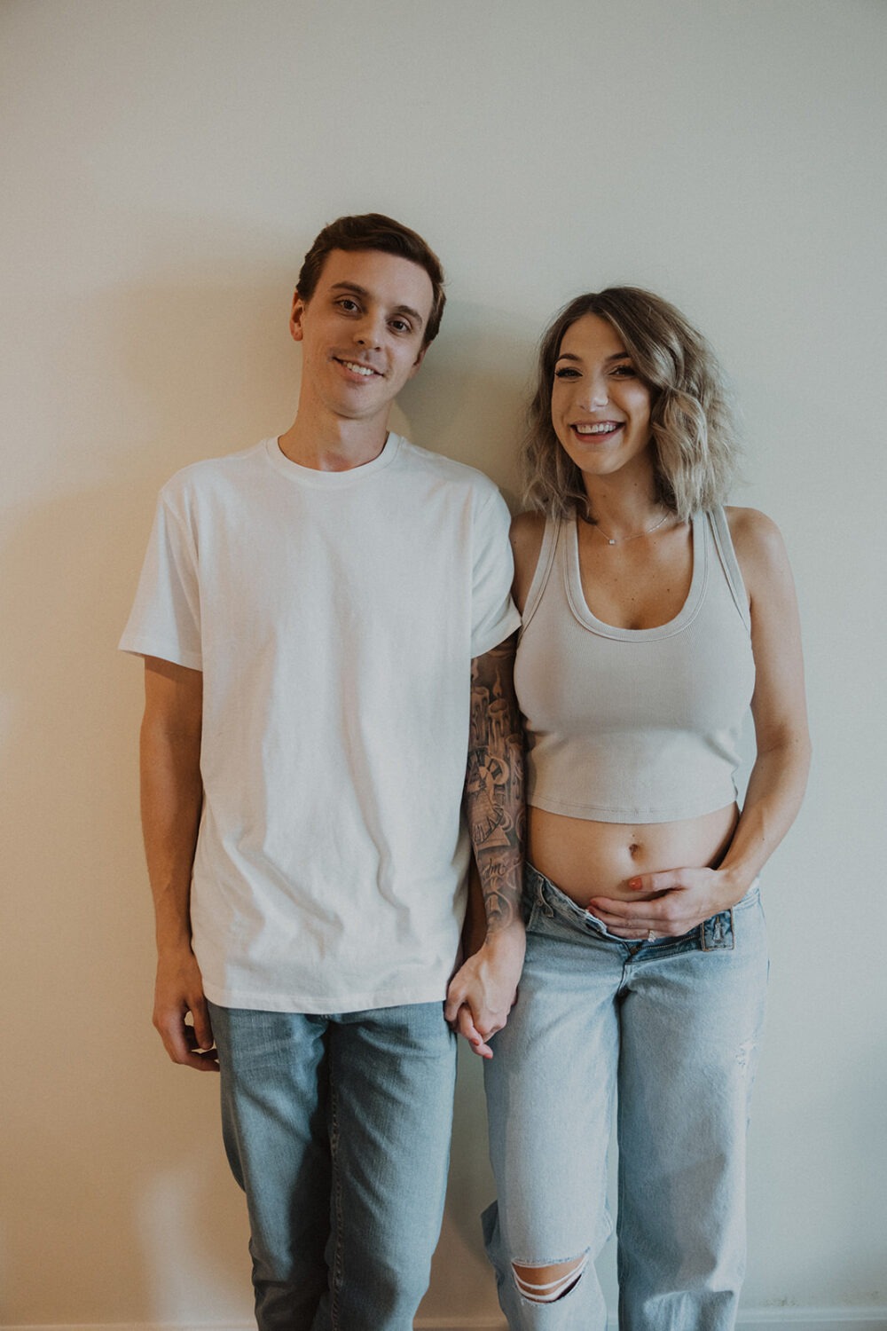 couple holds hands in their home while taking maternity photos