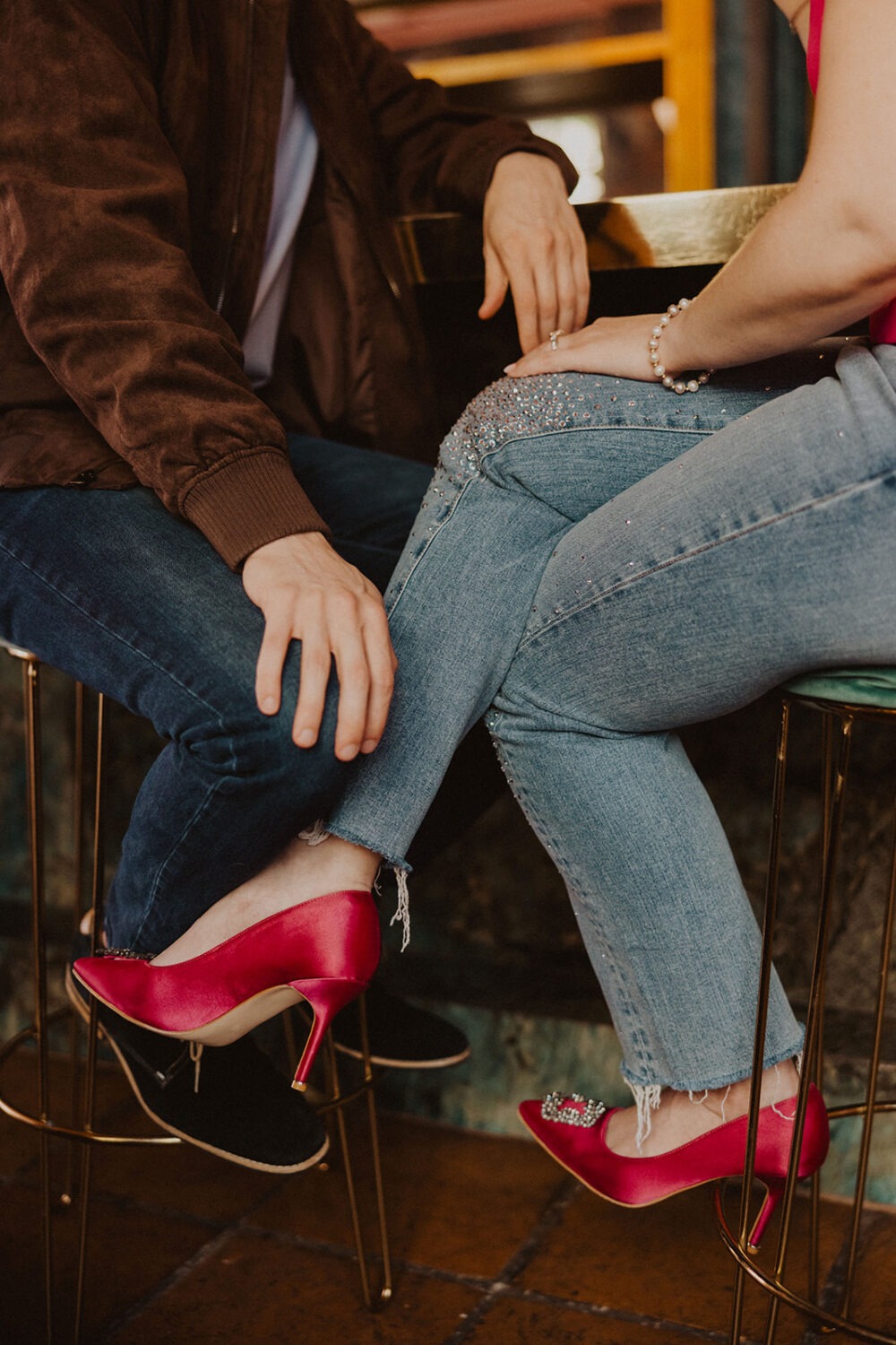 couple sitting together showing off hot pink high heels during engagement shoot