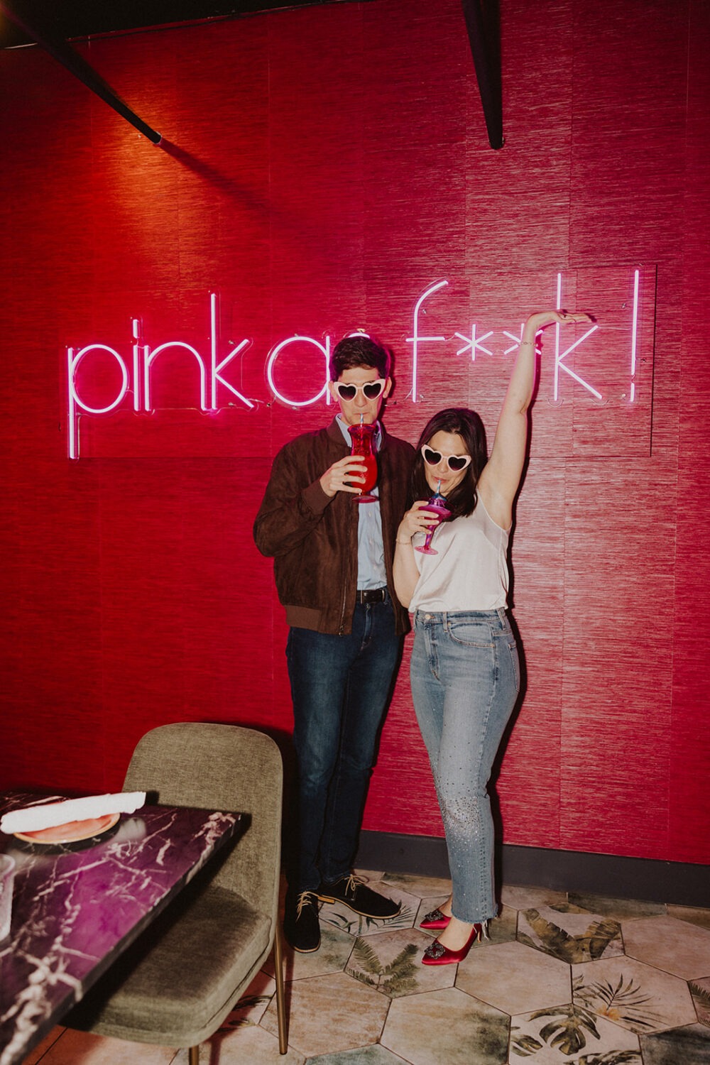 couple poses in front of hot pink wall during engagement shoot
