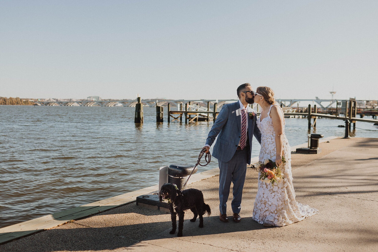 couple kissing with their dog alongside the water