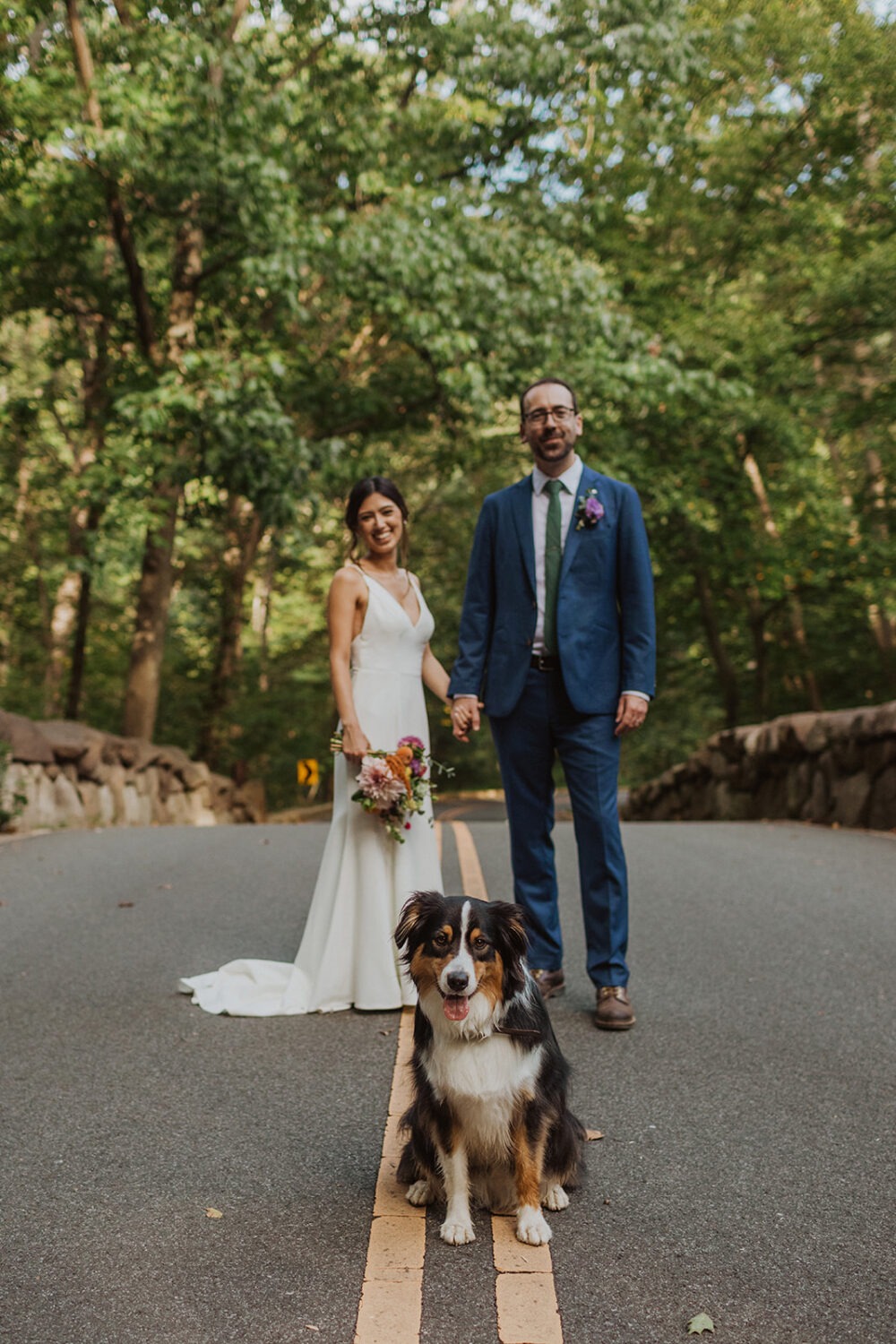 bride and groom pose with dog at park