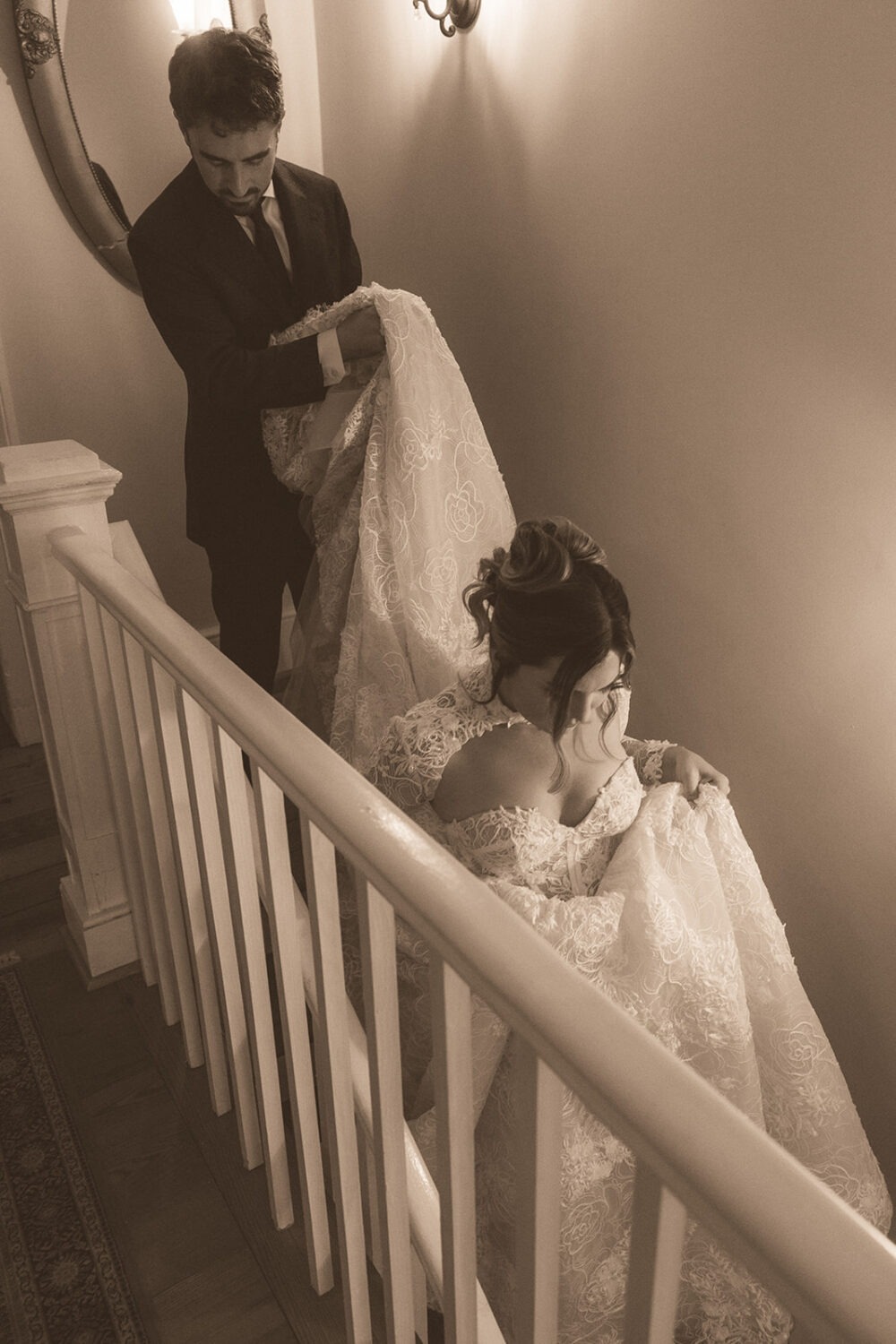groom helping carry brides dress down the stairs