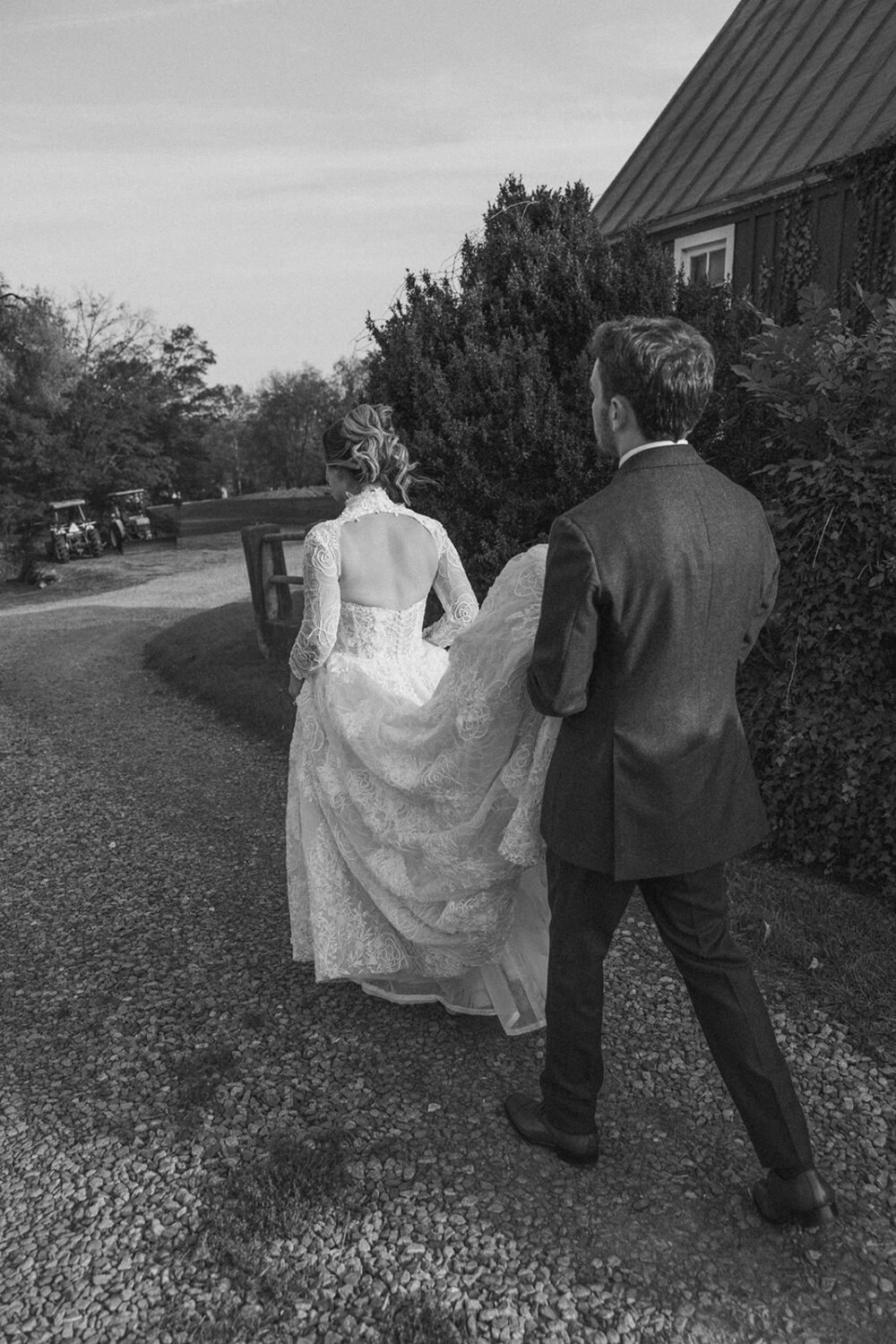 groom helps carry brides dress while walking along path
