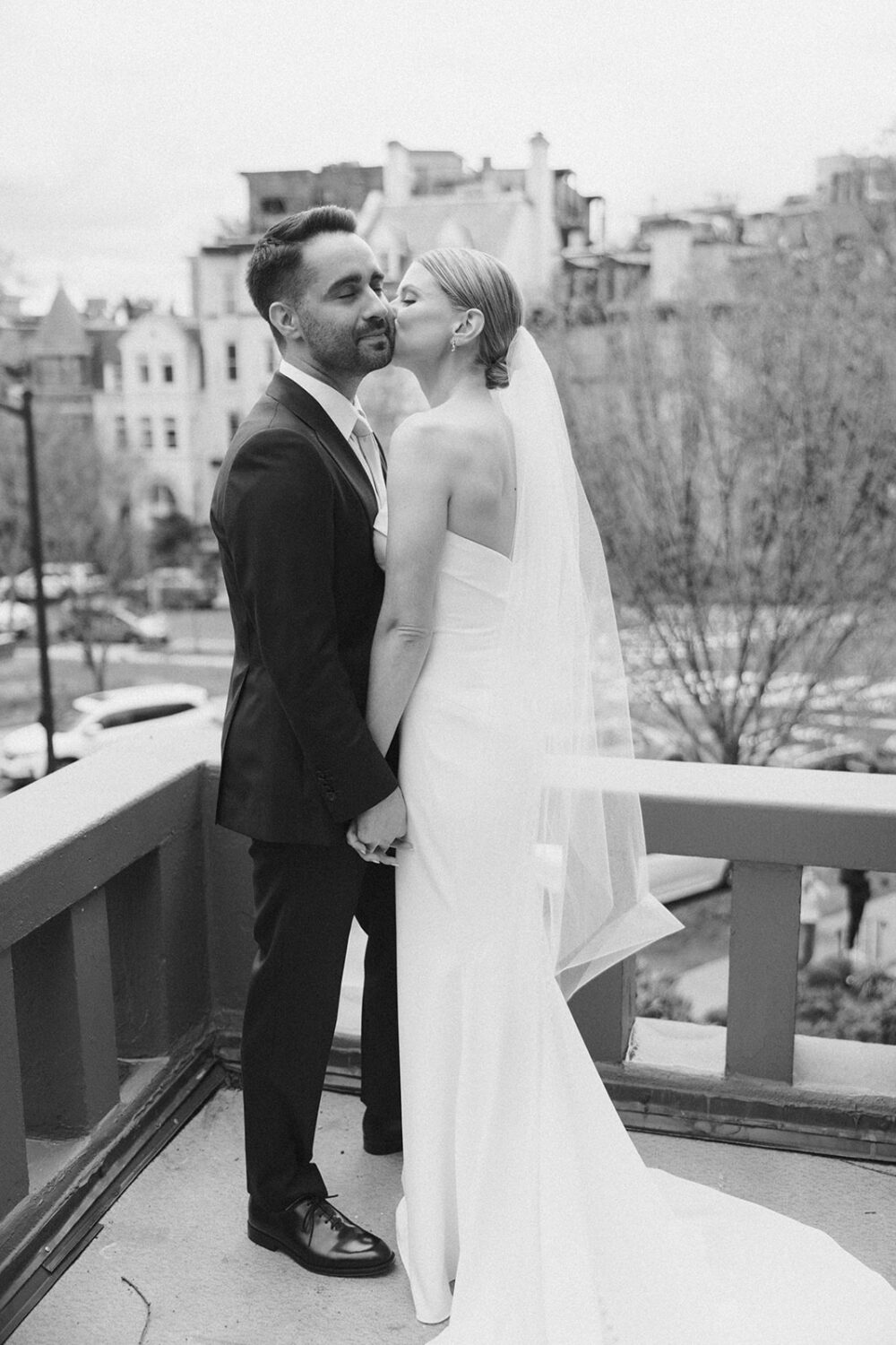 bride kisses groom on the cheek on terrance overlooking the city
